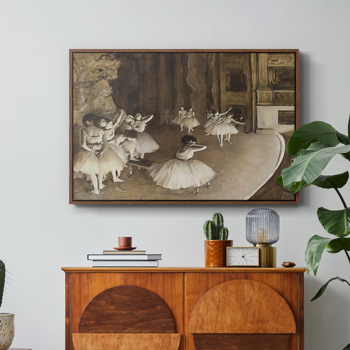 The Rehearsal of the Ballet Onstage, 1874 by Edgar Degas in a walnut floater framed canvas featuring ballerinas rehearsing on stage with set backdrop and lighting, displayed above a wood console cabinet.