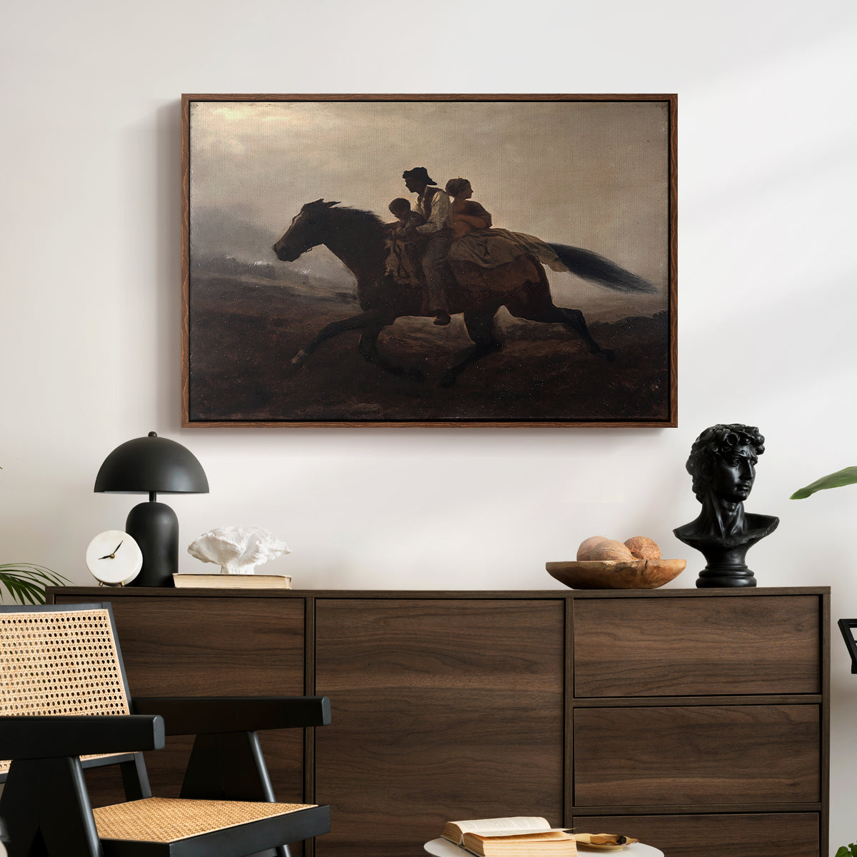 A Ride for Liberty – The Fugitive Slaves, c. 1862 by Eastman Johnson displayed in a walnut floater framed canvas above a dark wood credenza in an entryway.