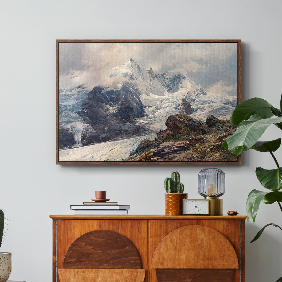 The Grossglockner, 1880 by Edward Theodore Compton in a walnut floater framed canvas featuring a towering mountain peak rising above rocky alpine landscape, displayed above a wood console cabinet.