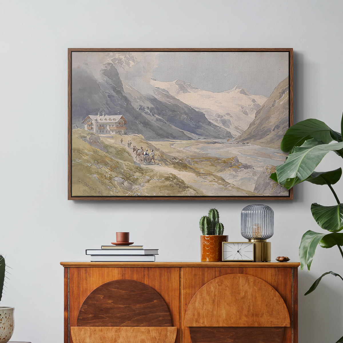 Shepherds (Pasterze), c. 1921 by Edward Theodore Compton in a walnut floater framed canvas featuring a small group of shepherds in alpine landscape with grazing animals, displayed above a wood console cabinet.