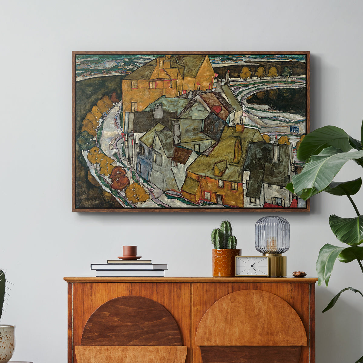 Crescent of Houses II (Island Town), 1915 by Egon Schiele in a walnut floater framed canvas featuring a curved row of colorful houses forming crescent shape along water, displayed above a wood console cabinet.