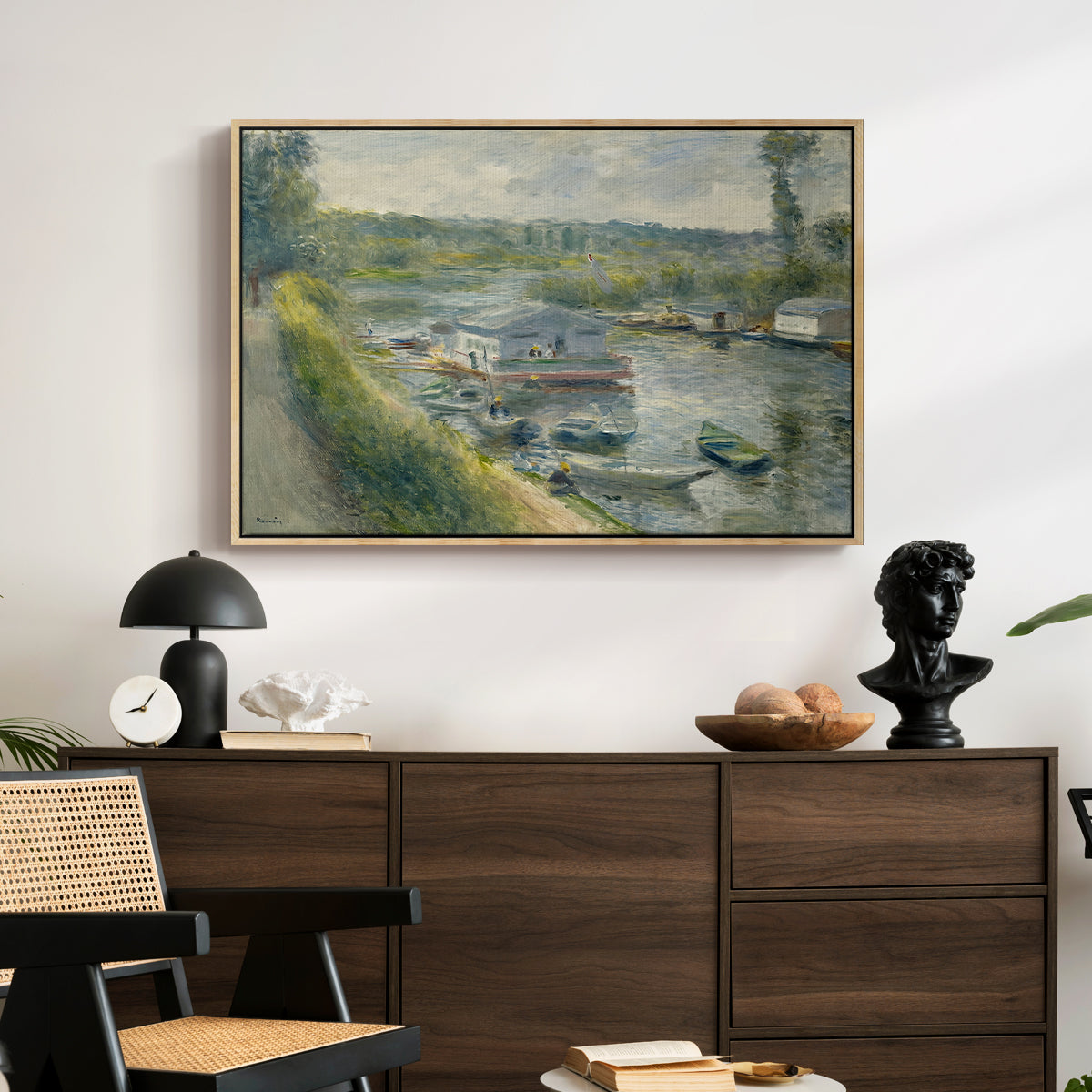 Wash-House Boat at Bas-Meudon, c. 1874 by Pierre-Auguste Renoir displayed in a natural wood floater framed canvas above a dark wood credenza in an entryway.