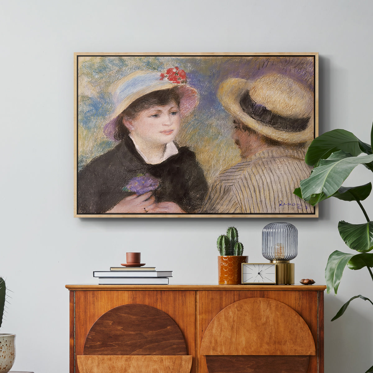 Boating Couple (Aline Charigot and Renoir), c. 1881 by Pierre-Auguste Renoir in a natural wood floater framed canvas featuring a close-up of a couple seated together outdoors with hats and soft sunlight, displayed above a wood console cabinet.
