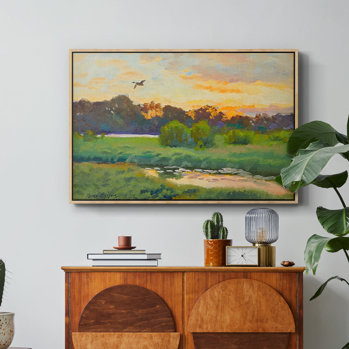 Flying Duck at Sunset, 1924 by Bruno Liljefors in a natural wood floater framed canvas featuring a wild duck flying over a sunset marsh with trees, displayed above a wood console cabinet.