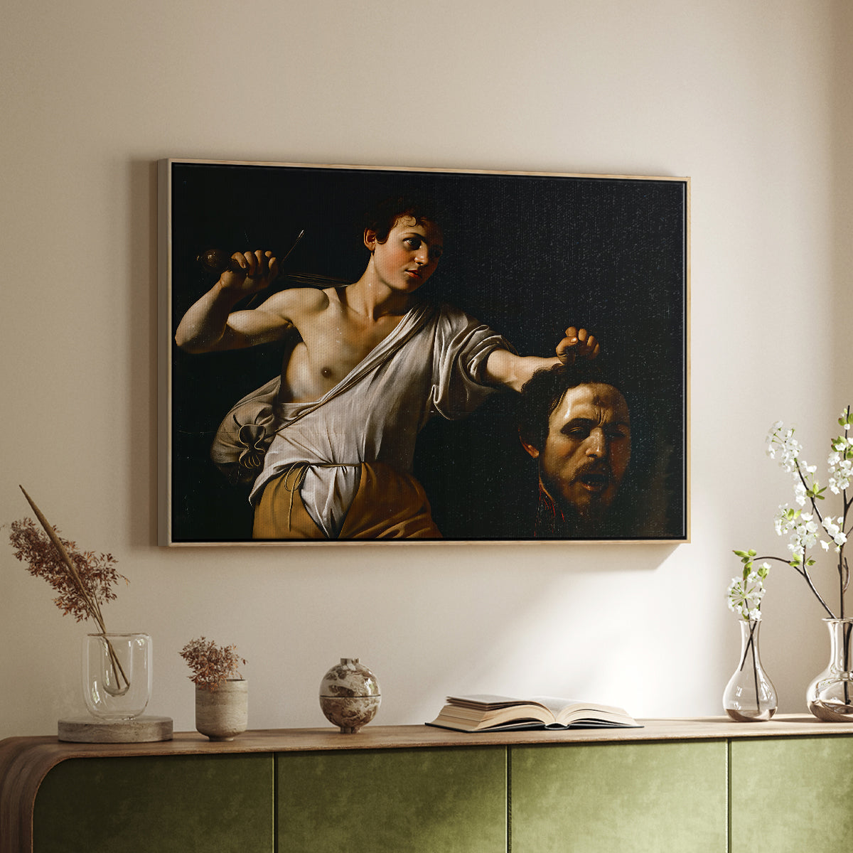 Natural wood floater framed canvas of David with the Head of Goliath (Vienna Version), c. 1607 by Caravaggio, featuring a biblical scene of David gripping Goliath's head with dramatic lighting above a sideboard in a softly lit hallway.