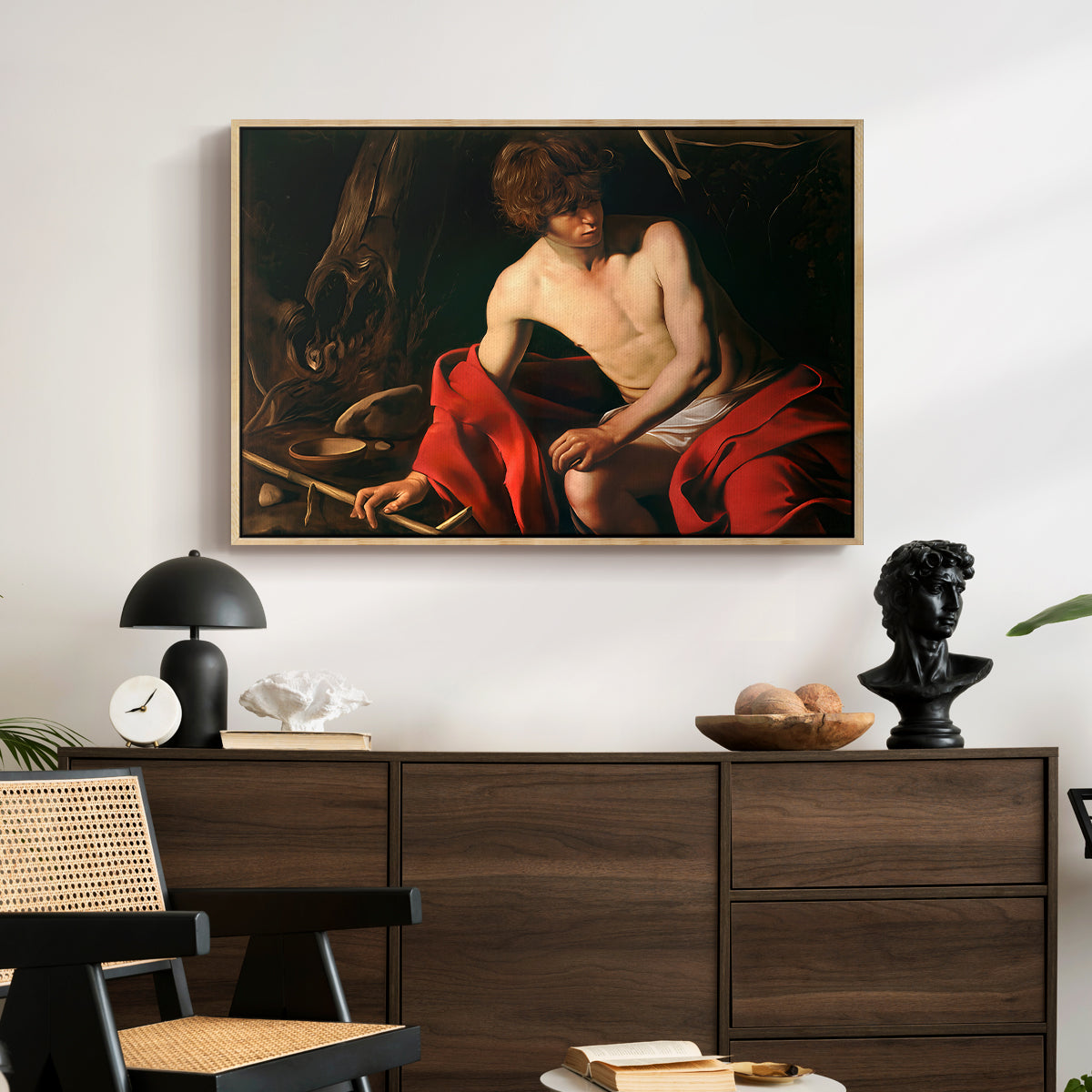 Saint John the Baptist in the Wilderness, c. 1603-1604 by Caravaggio displayed in a natural wood floater framed canvas above a dark wood credenza in an entryway.