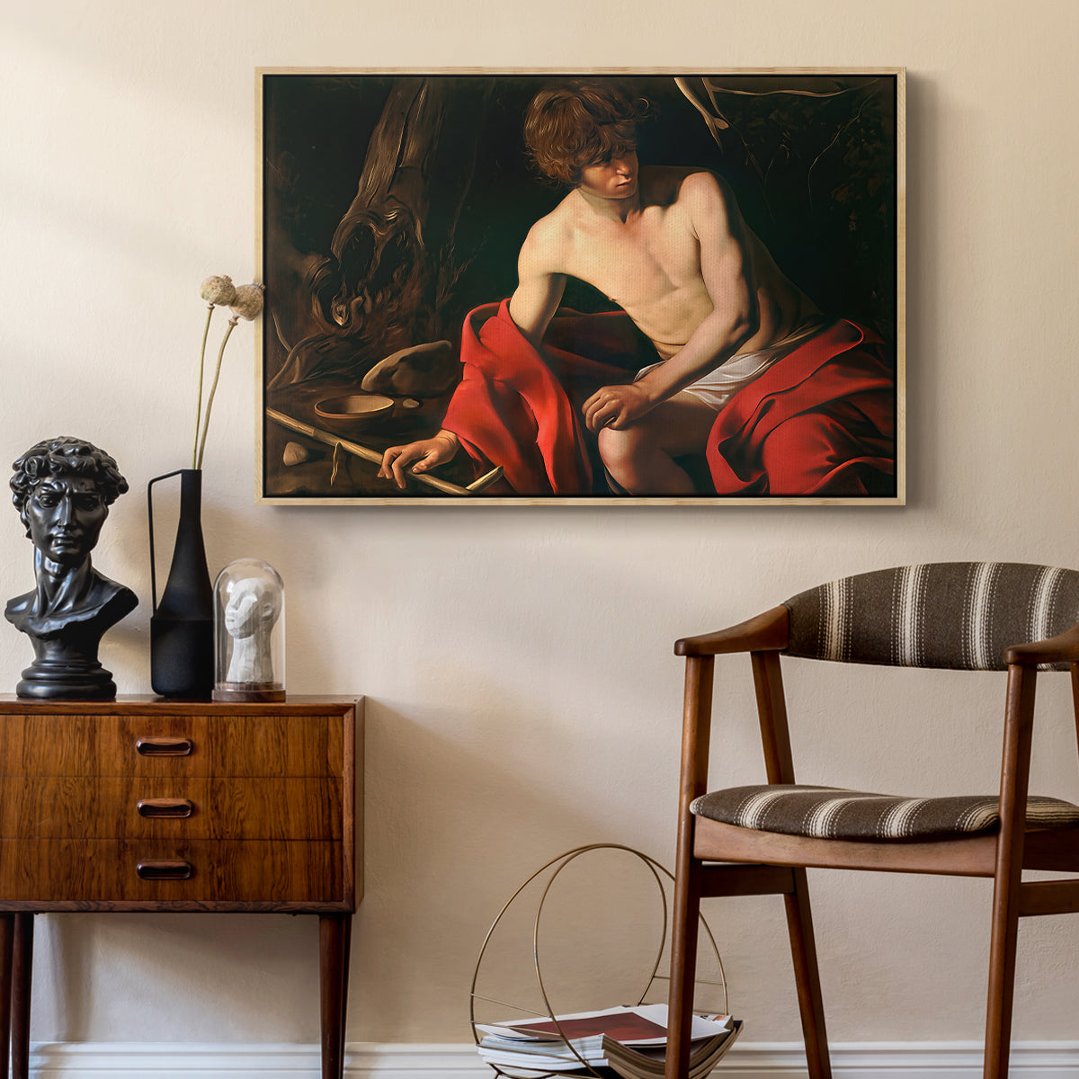 Saint John the Baptist in the Wilderness, c. 1603-1604 by Caravaggio as a natural wood floater framed canvas featuring a biblical youth seated outdoors with symbolic staff and minimal landscape, styled above a mid-century console in a contemporary living area.