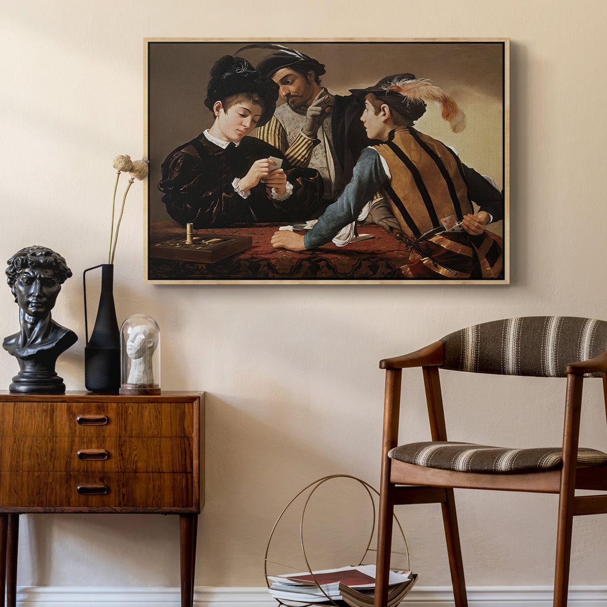 The Cardsharps, c. 1594 by Caravaggio as a natural wood floater framed canvas featuring a young men playing cards with one cheating and another watching closely, styled above a mid-century console in a contemporary living area.