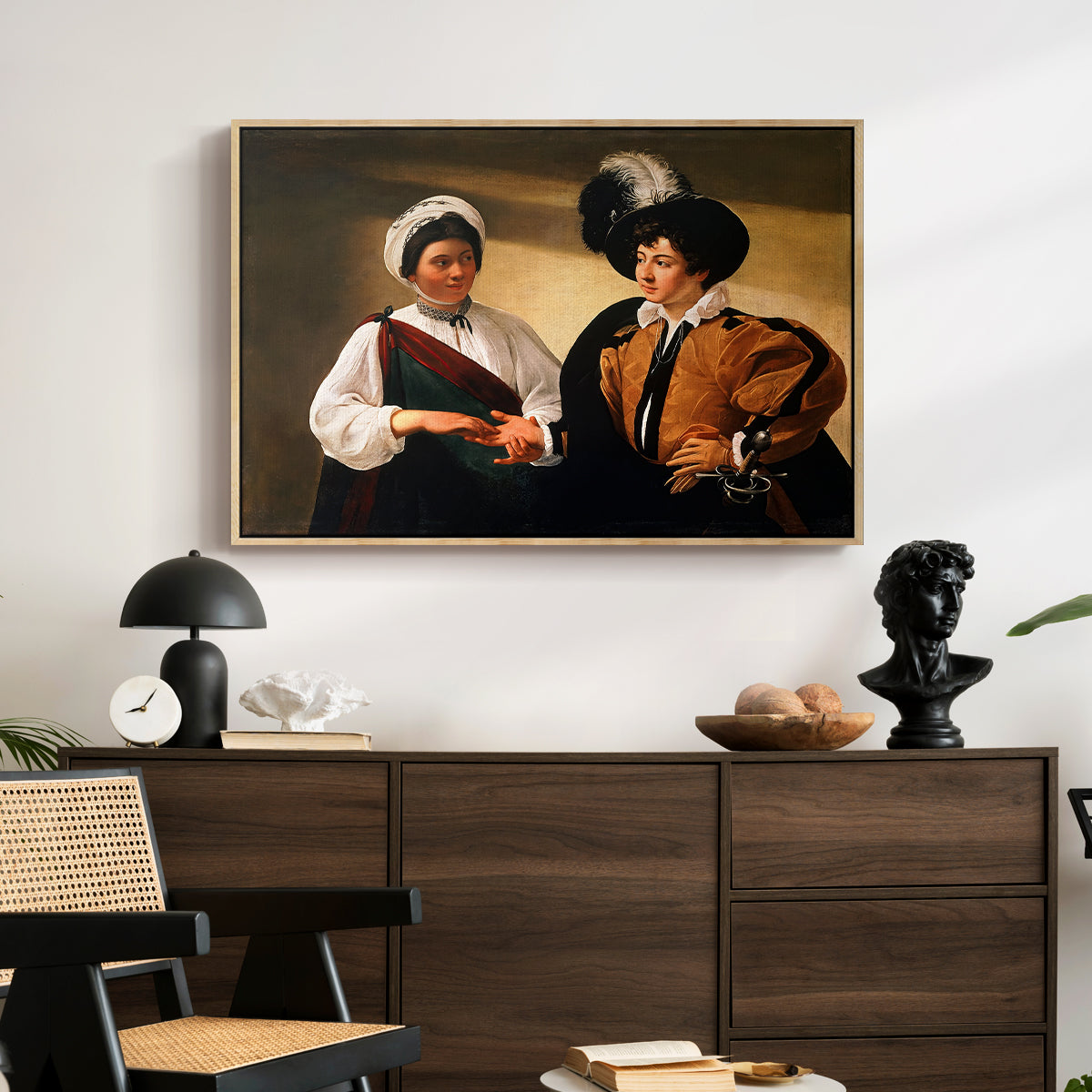 The Fortune Teller (Louvre Version), c. 1595 by Caravaggio displayed in a natural wood floater framed canvas above a dark wood credenza in an entryway.