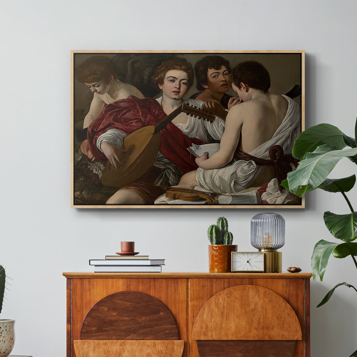 The Musicians, c. 1595 by Caravaggio in a natural wood floater framed canvas featuring a group of young men gathered together playing music with instruments, displayed above a wood console cabinet.