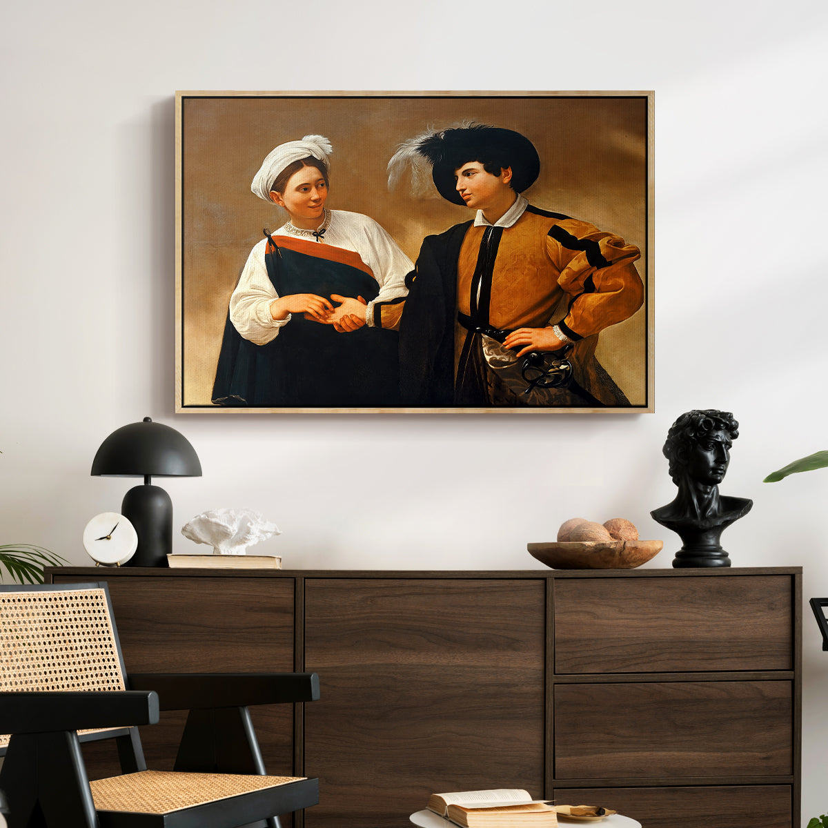 The Fortune Teller (Capitoline Version), c. 1599 by Caravaggio displayed in a natural wood floater framed canvas above a dark wood credenza in an entryway.