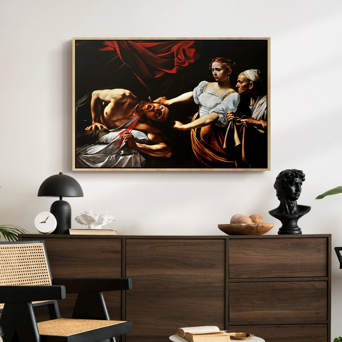 Judith Beheading Holofernes, c. 1599 by Caravaggio displayed in a natural wood floater framed canvas above a dark wood credenza in an entryway.