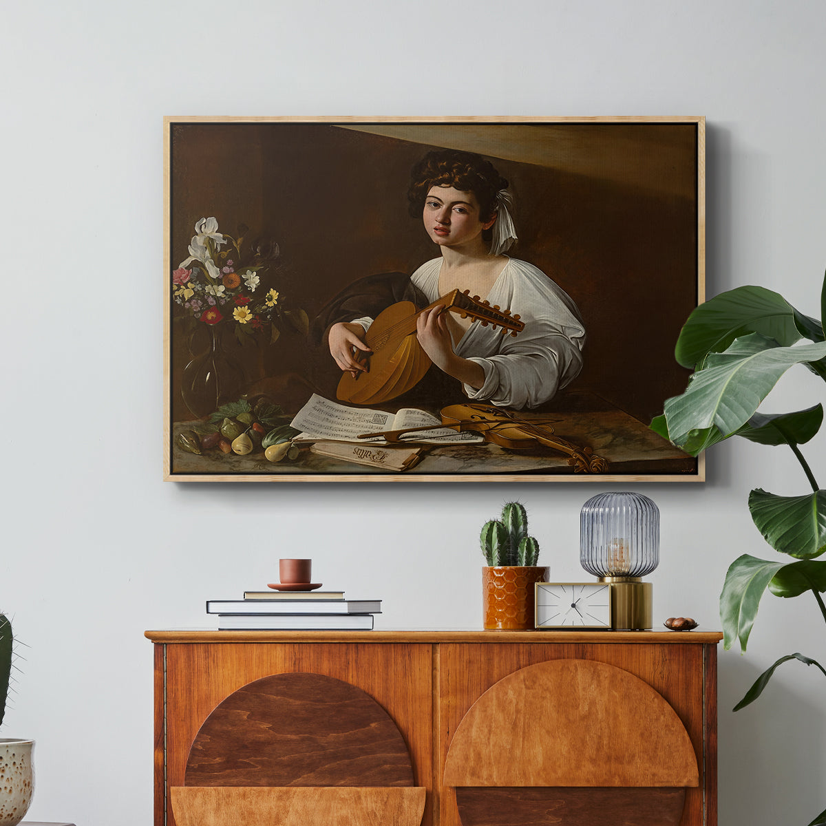 The Lute Player (Hermitage Version), c. 1596 by Caravaggio in a natural wood floater framed canvas featuring a young musician playing lute beside table with fruit and sheet music, displayed above a wood console cabinet.