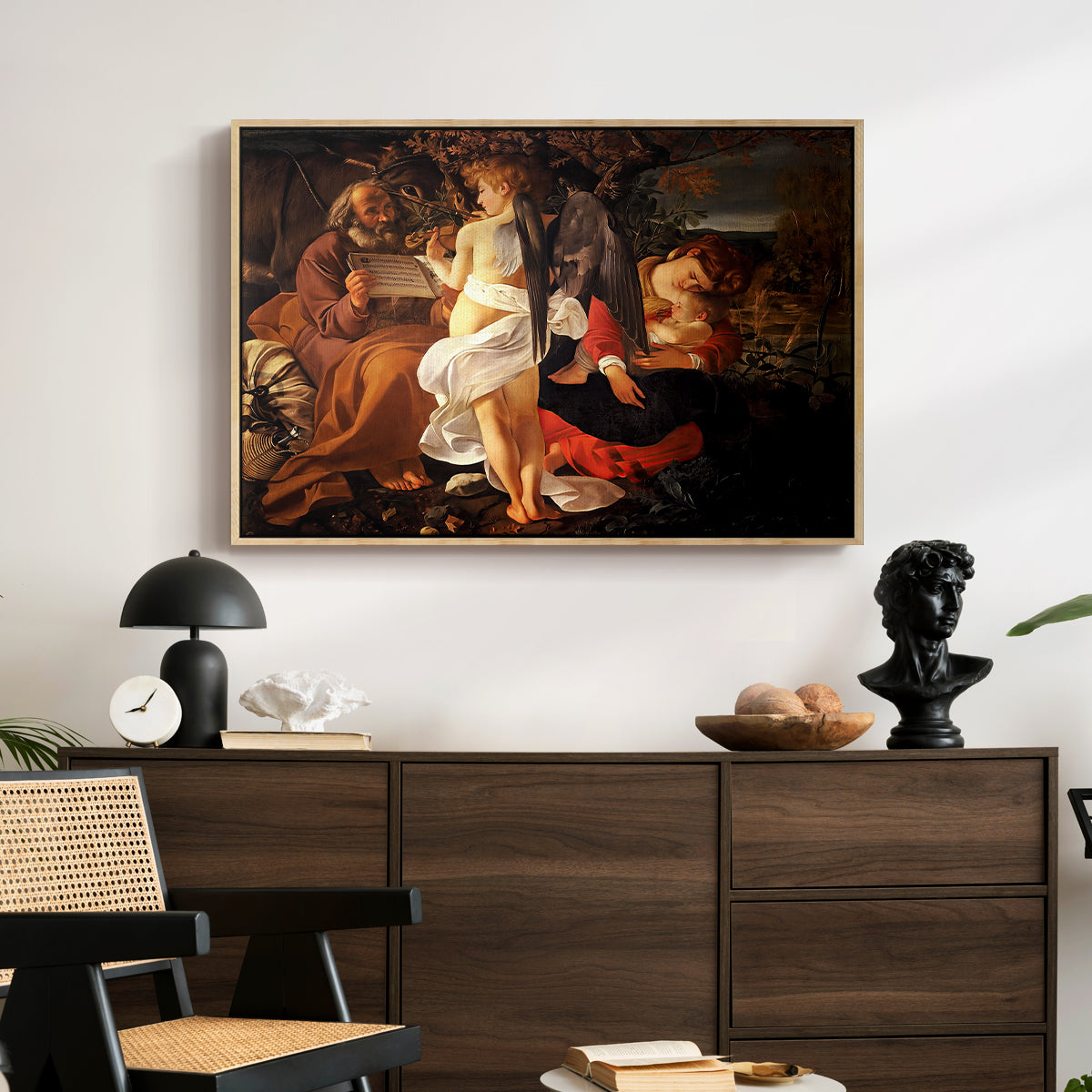 Rest on the Flight into Egypt, c. 1597 by Caravaggio displayed in a natural wood floater framed canvas above a dark wood credenza in an entryway.