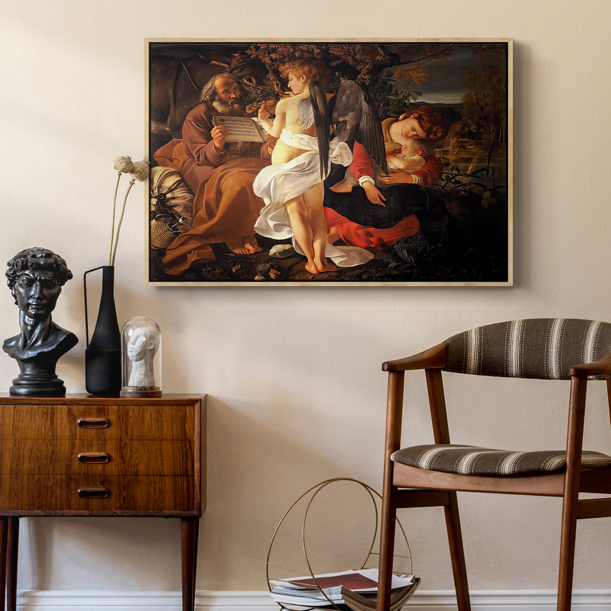 Rest on the Flight into Egypt, c. 1597 by Caravaggio as a natural wood floater framed canvas featuring a peaceful religious moment with figures reclining in natural setting, styled above a mid-century console in a contemporary living area.