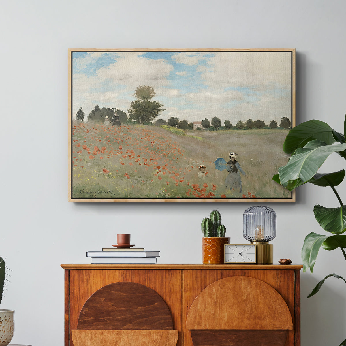 The Poppy Field near Argenteuil, 1873 by Claude Monet in a natural wood floater framed canvas featuring a field of red poppies with figures walking across rolling landscape, displayed above a wood console cabinet.