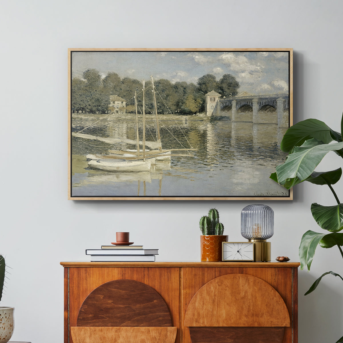 The Bridge at Argenteuil, 1874 by Claude Monet in a natural wood floater framed canvas featuring a bridge spanning river with sailboats and reflections in water, displayed above a wood console cabinet.