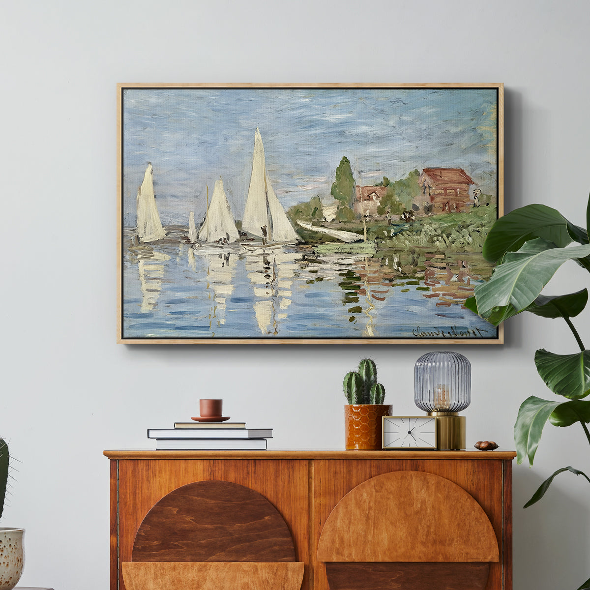 Regatta at Argenteuil, 1872 by Claude Monet in a natural wood floater framed canvas featuring colorful sailboats racing across river under bright sky, displayed above a wood console cabinet.