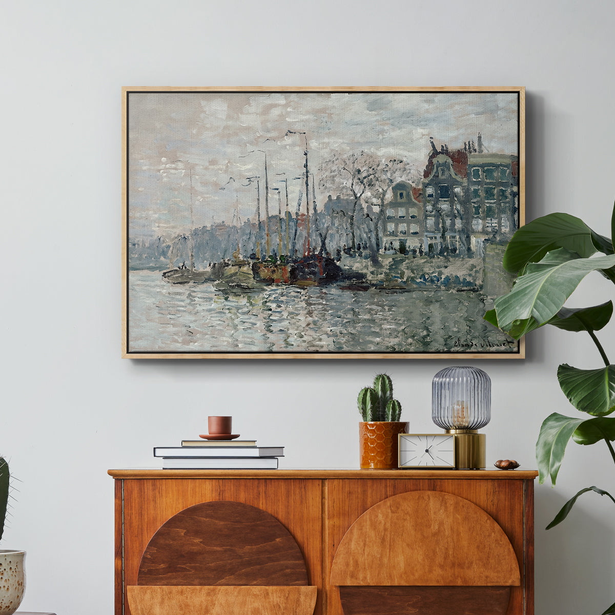View of the Prins Hendrikkade and Kromme Waal in Amsterdam, 1874 by Claude Monet in a natural wood floater framed canvas featuring a canal scene with boats and buildings lining waterfront in Amsterdam, displayed above a wood console cabinet.
