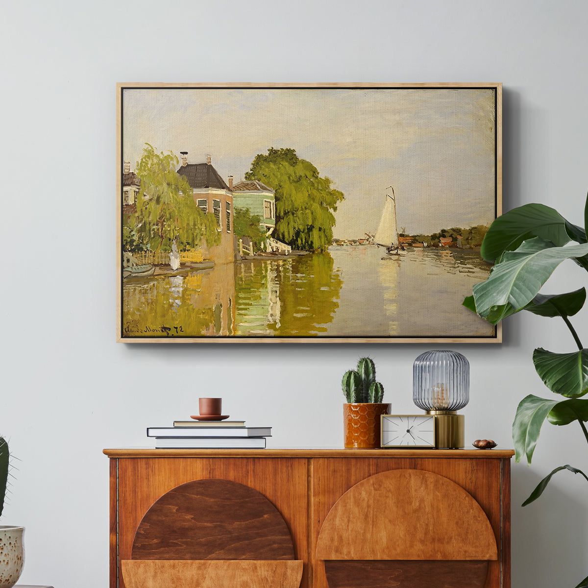 Houses on the Achterzaan, 1871 by Claude Monet in a natural wood floater framed canvas featuring colorful houses reflected in calm river surrounded by greenery, displayed above a wood console cabinet.