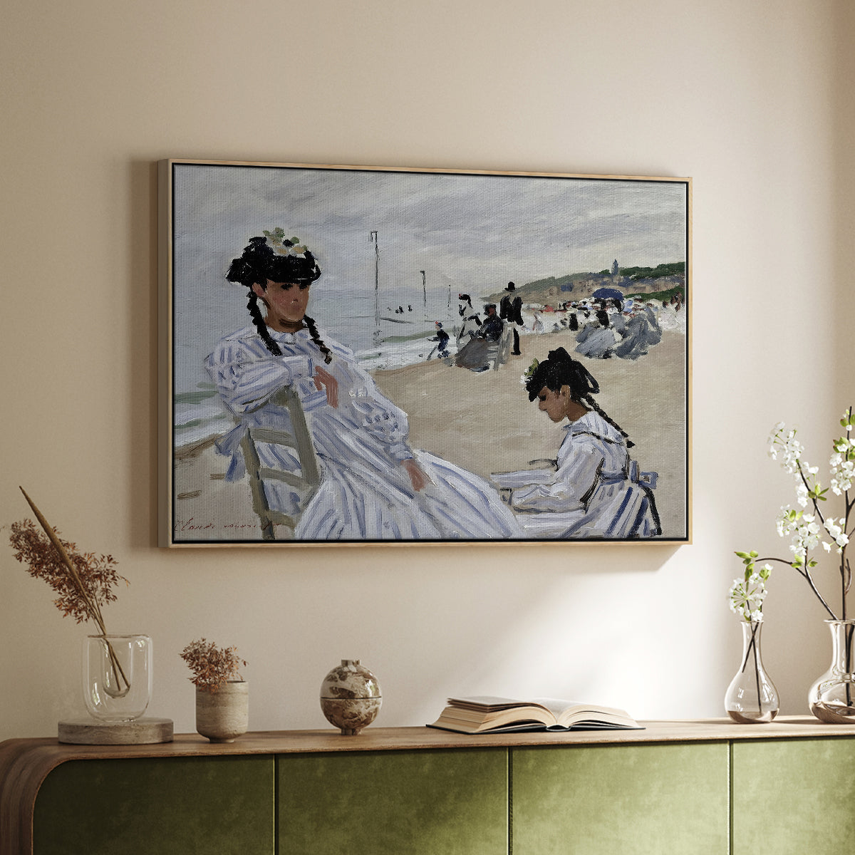 Natural wood floater framed canvas of On the Beach at Trouville, 1870 by Claude Monet, featuring an impressionist seaside scene with women in dresses and hats above a sideboard in a softly lit hallway.