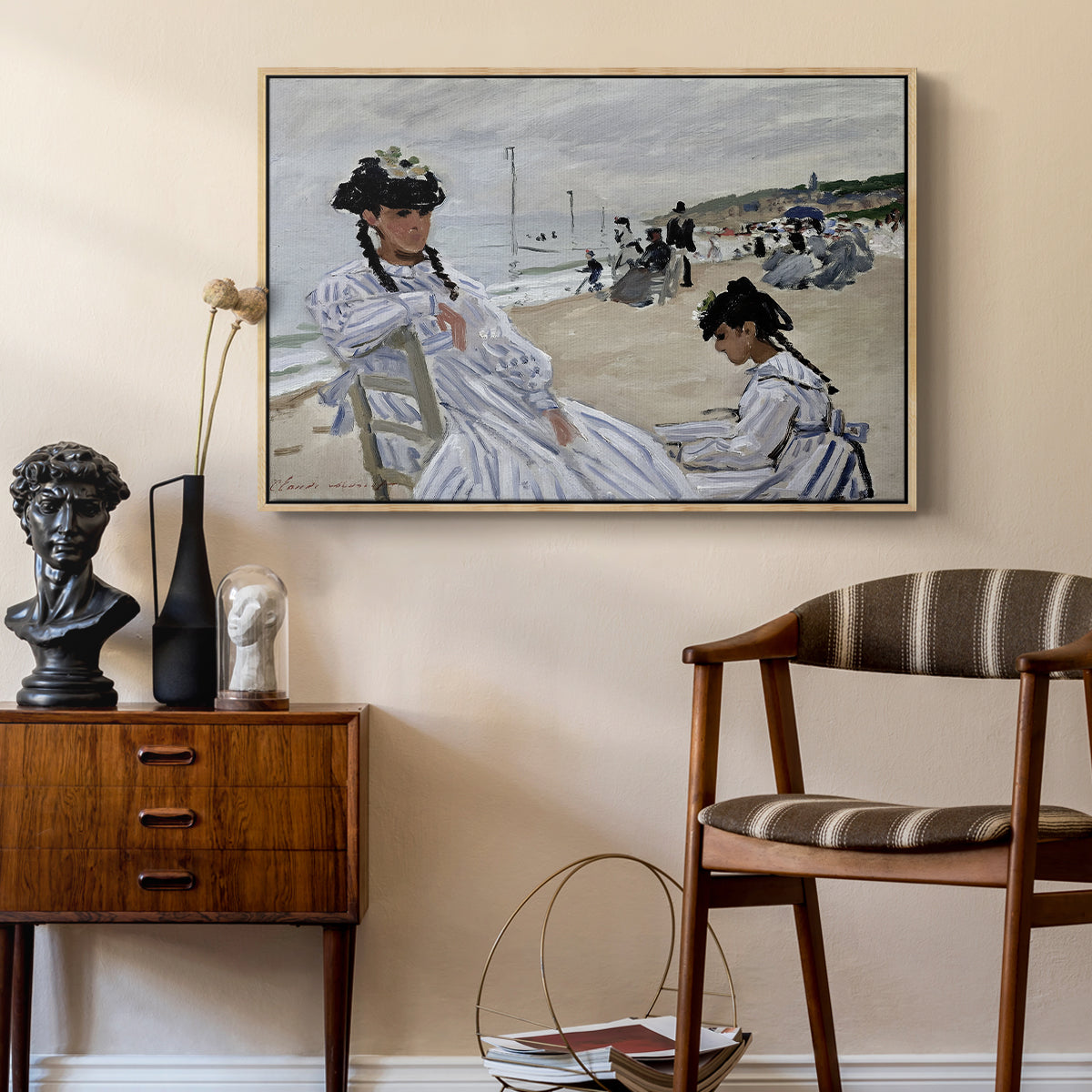 On the Beach at Trouville, 1870 by Claude Monet as a natural wood floater framed canvas featuring a beach setting with people relaxing under umbrellas, styled above a mid-century console in a contemporary living area.