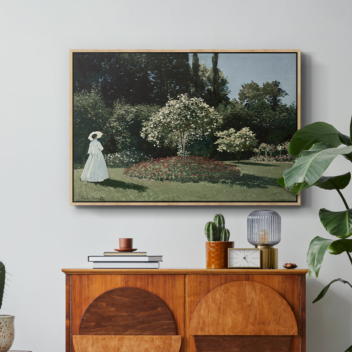 Woman in the Garden, Sainte-Adresse, 1867 by Claude Monet in a natural wood floater framed canvas featuring a woman standing in garden surrounded by flowers and greenery, displayed above a wood console cabinet.