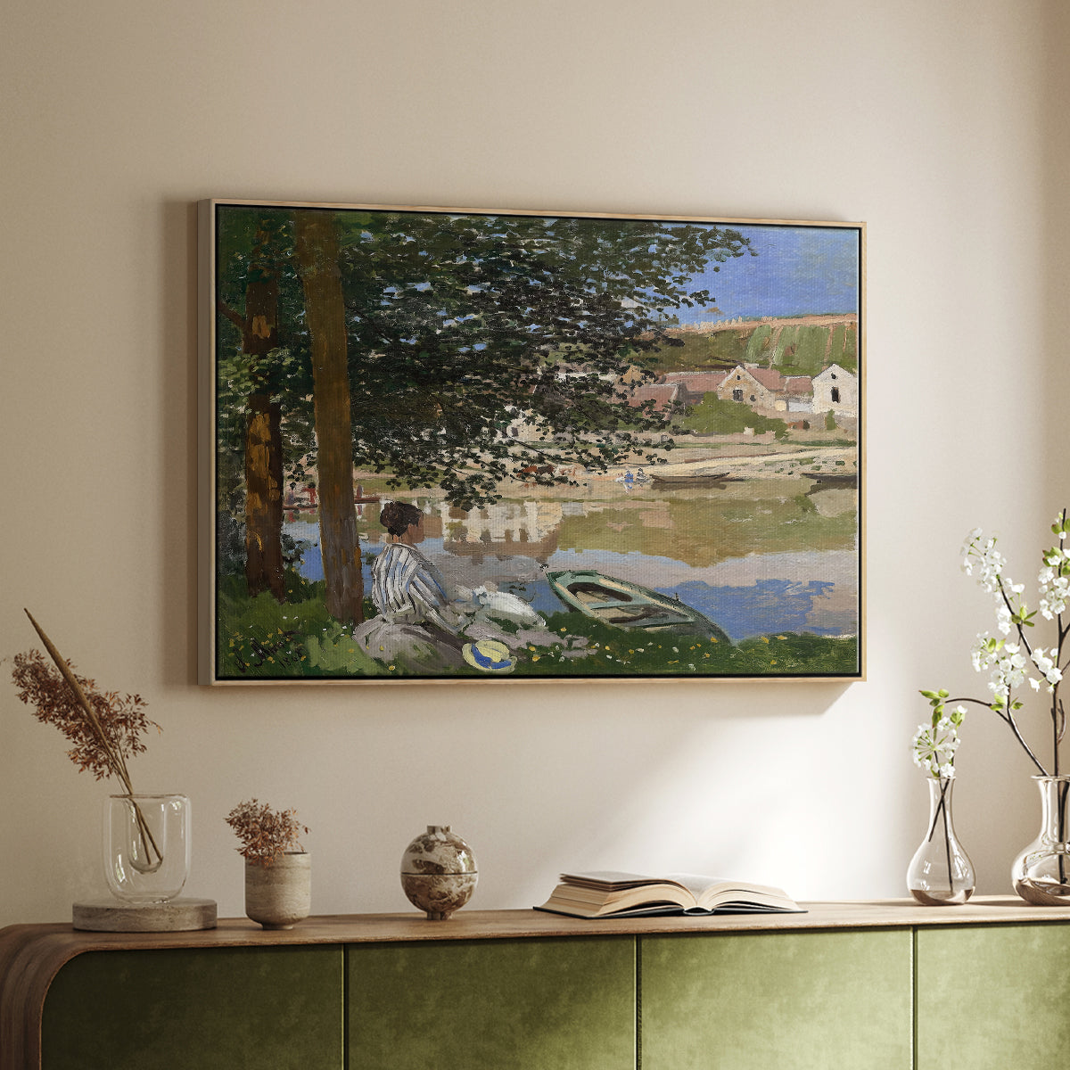 Natural wood floater framed canvas of On the Bank of the Seine, Bennecourt, 1868 by Claude Monet, featuring a peaceful riverside scene with figures resting in grassy area by water above a sideboard in a softly lit hallway.