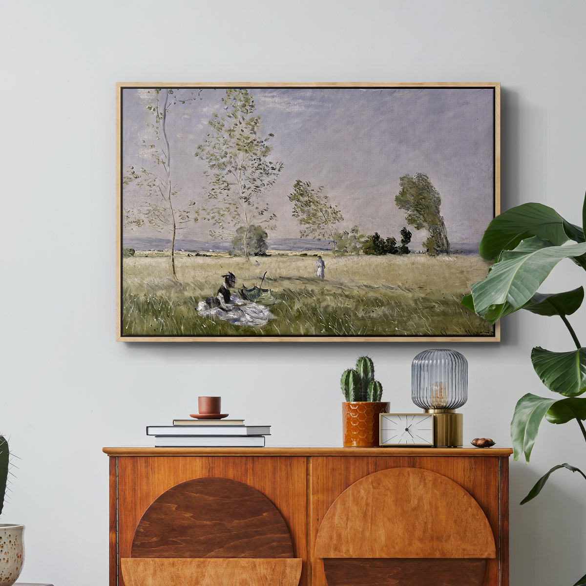 Summer (L'ete), 1874 by Claude Monet in a natural wood floater framed canvas featuring a woman seated in grassy field beneath tree in bright summer landscape, displayed above a wood console cabinet.
