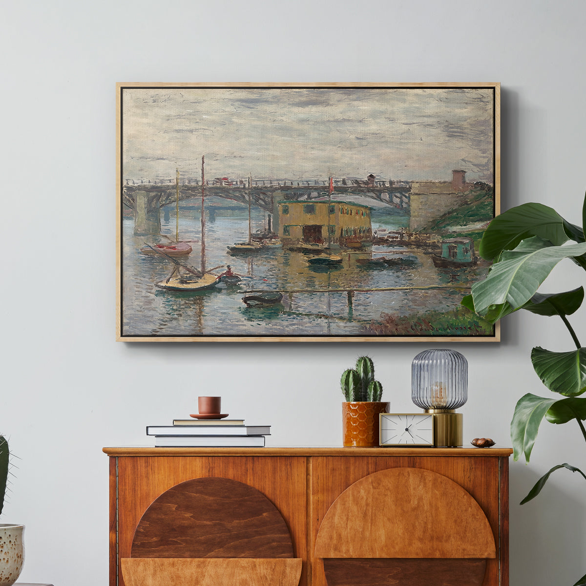 Bridge at Argenteuil on a Gray Day, c. 1876 by Claude Monet in a natural wood floater framed canvas featuring a bridge crossing river under gray sky with muted reflections, displayed above a wood console cabinet.
