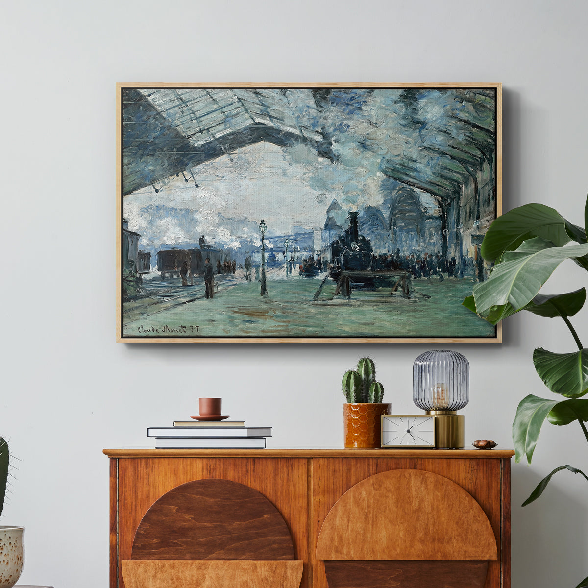 The Saint-Lazare Station, 1877 by Claude Monet in a natural wood floater framed canvas featuring trains arriving under large arched station roof with billowing steam, displayed above a wood console cabinet.