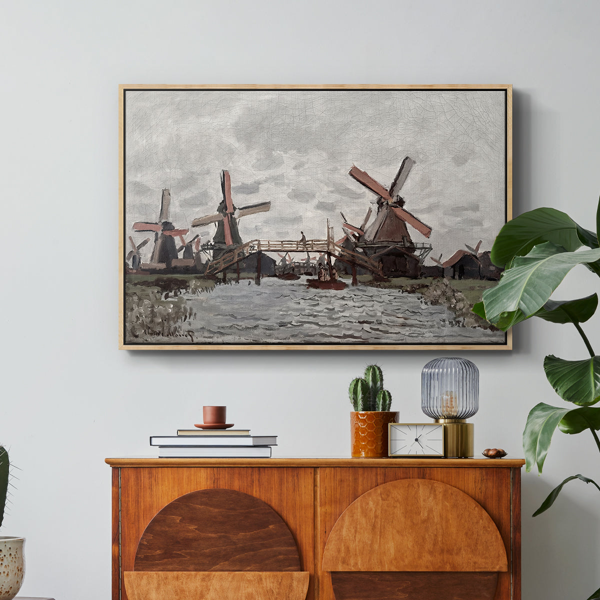 Windmills near Zaandam, 1871 by Claude Monet in a natural wood floater framed canvas featuring windmills standing beside water under open sky in rural landscape, displayed above a wood console cabinet.