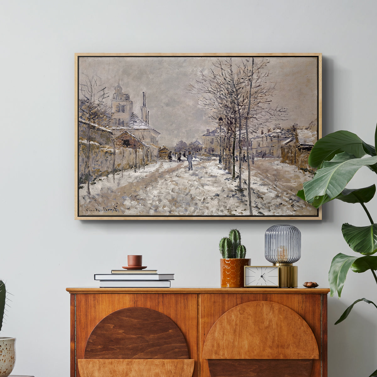 The Boulevard de Pontoise at Argenteuil, Snow Effect, 1875 by Claude Monet in a natural wood floater framed canvas featuring a snow-covered street lined with trees and buildings under winter sky, displayed above a wood console cabinet.