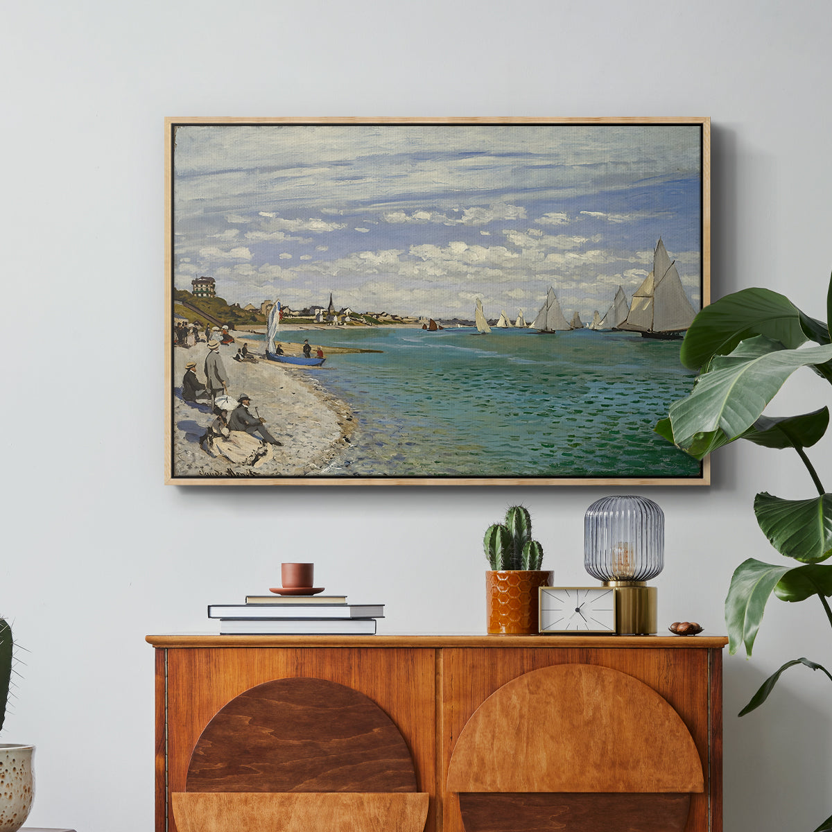 Regatta at Sainte-Adresse, 1867 by Claude Monet in a natural wood floater framed canvas featuring sailboats gathered near shore with flags and spectators along coastline, displayed above a wood console cabinet.