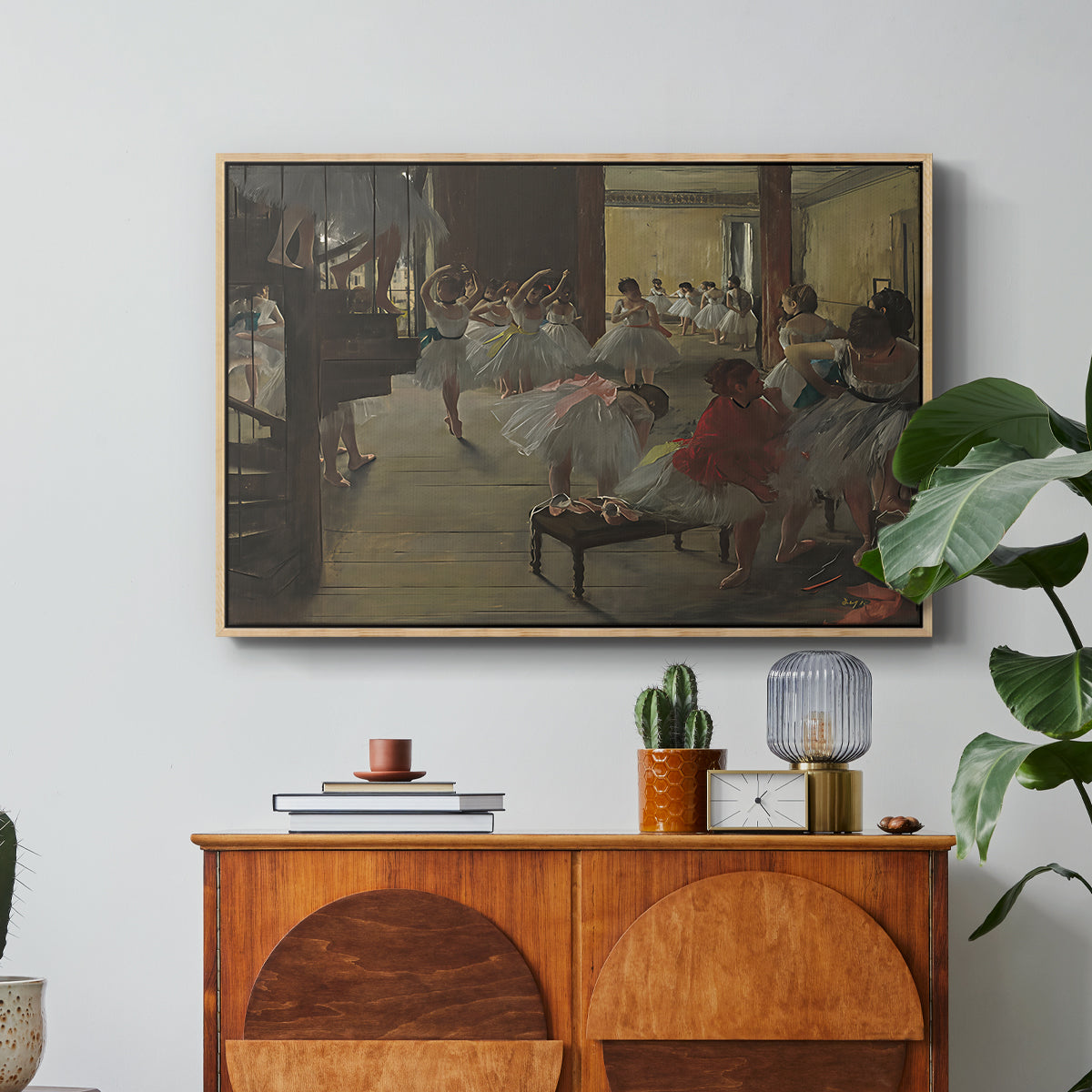 The Dance Class, c. 1873 by Edgar Degas in a natural wood floater framed canvas featuring ballerinas practicing in studio with instructor observing nearby, displayed above a wood console cabinet.