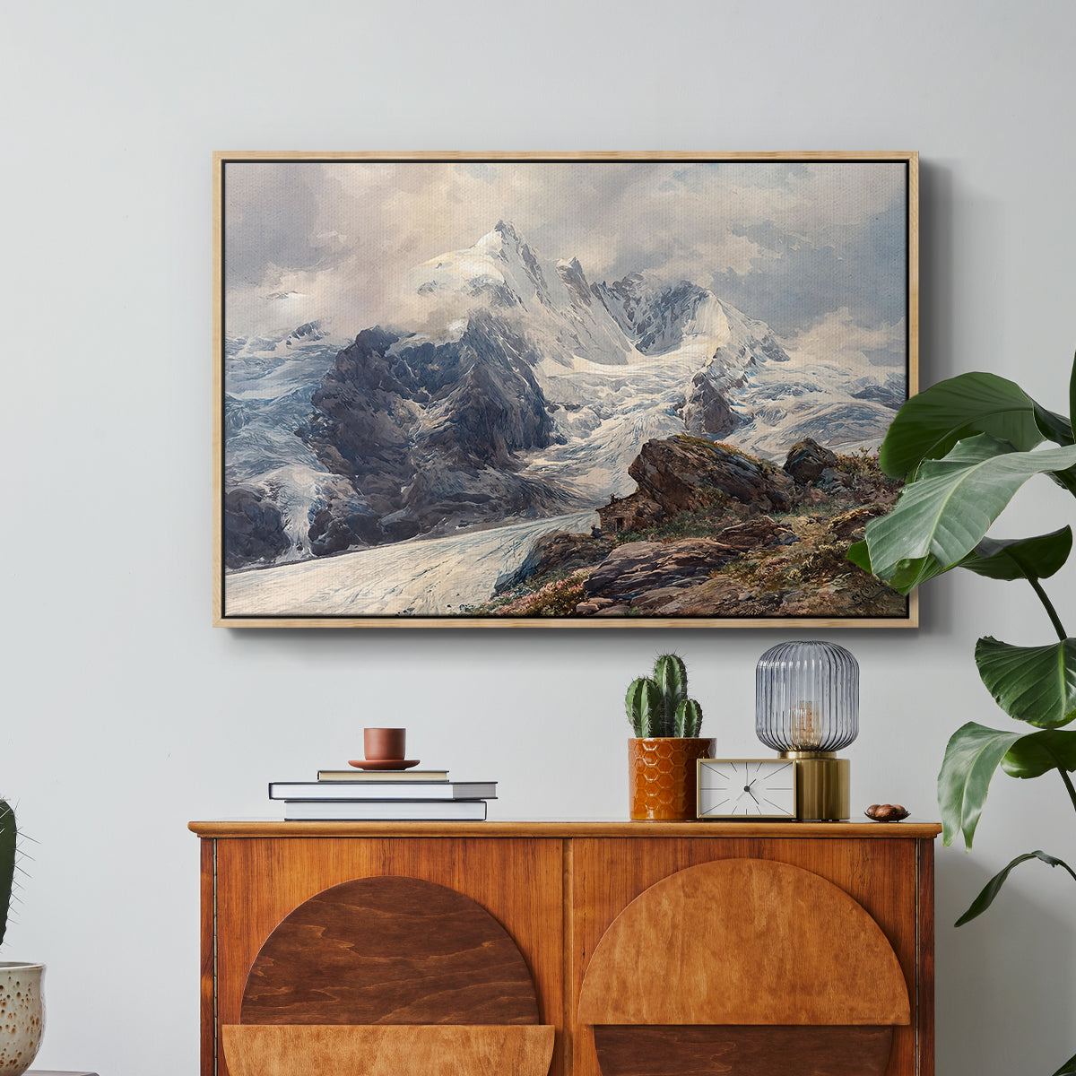 The Grossglockner, 1880 by Edward Theodore Compton in a natural wood floater framed canvas featuring a towering mountain peak rising above rocky alpine landscape, displayed above a wood console cabinet.