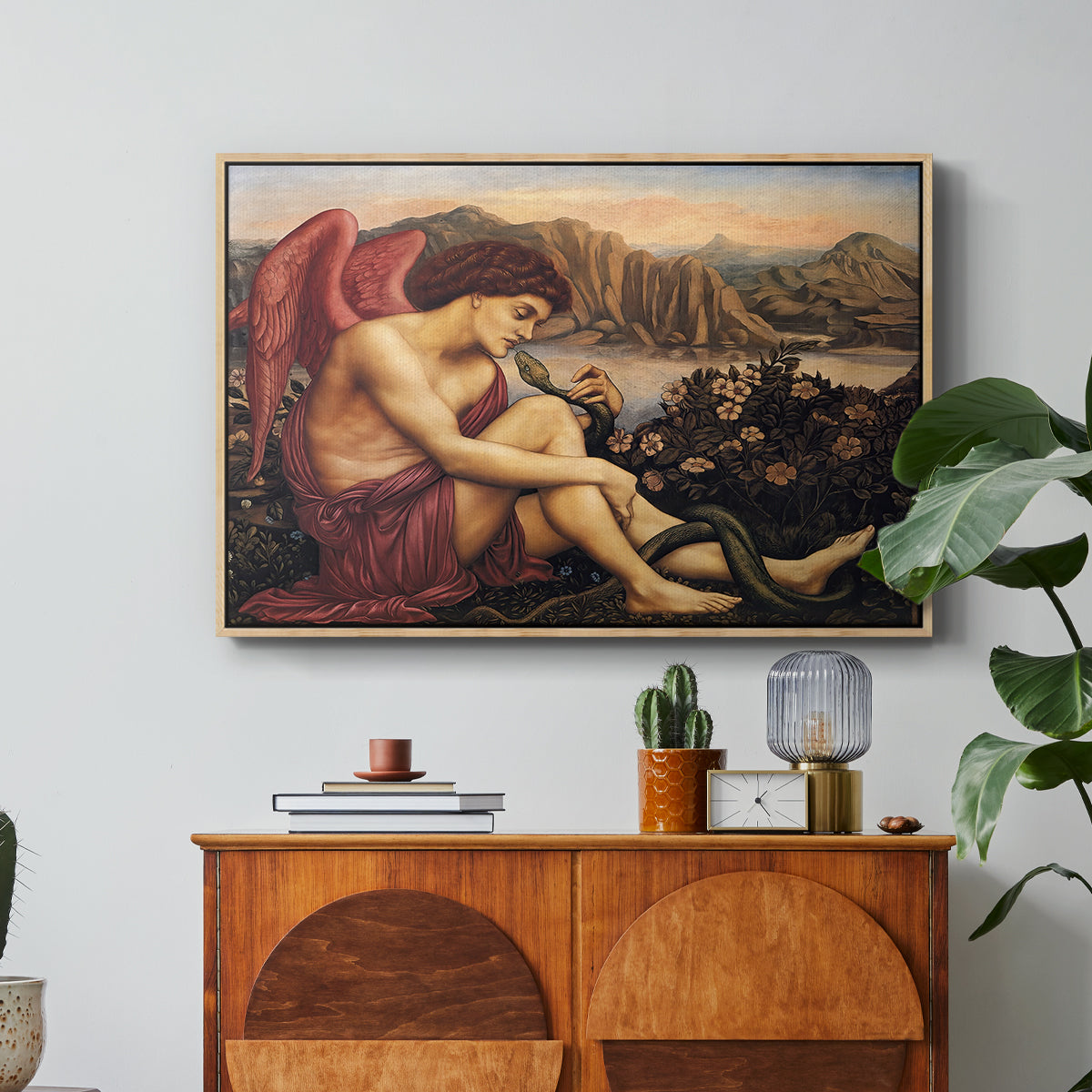 The Angel with the Serpent, c. 1870-1875 by Evelyn De Morgan in a natural wood floater framed canvas featuring an angelic figure confronting serpent in symbolic battle of good and evil, displayed above a wood console cabinet.