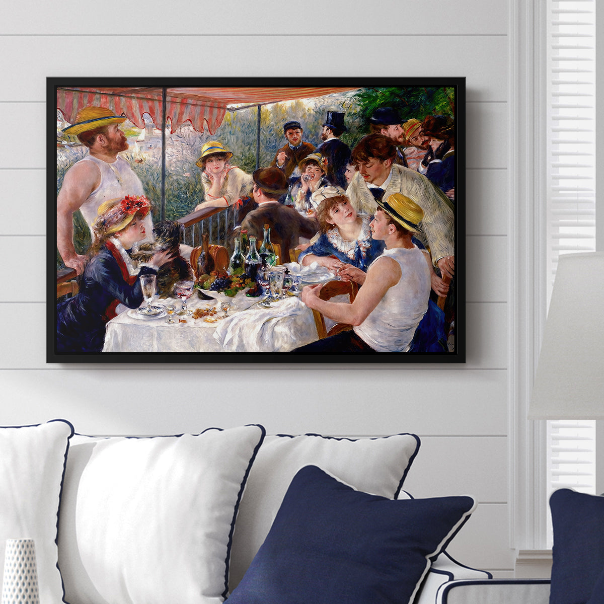 Luncheon of the Boating Party (Le Déjeuner des canotiers), 1880-1881 by Pierre-Auguste Renoir displayed above a sofa in a living room in a black floater frame, featuring a lively gathering of men and women eating and socializing at outdoor table.