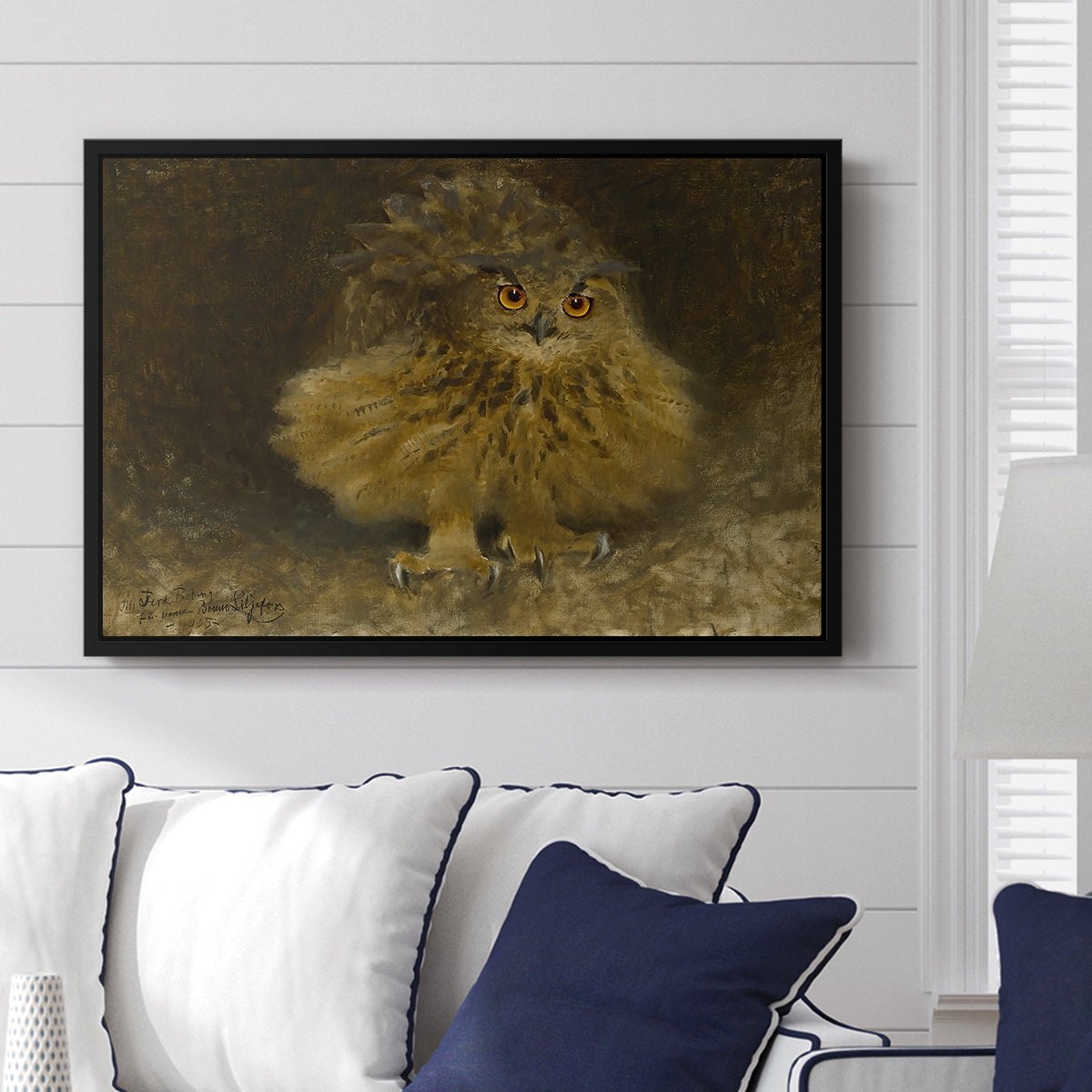 An Eagle Owl (Berguv), 1905 by Bruno Liljefors displayed above a sofa in a living room in a black floater frame, featuring a detailed wildlife painting of eagle owl with piercing eyes in darkness.