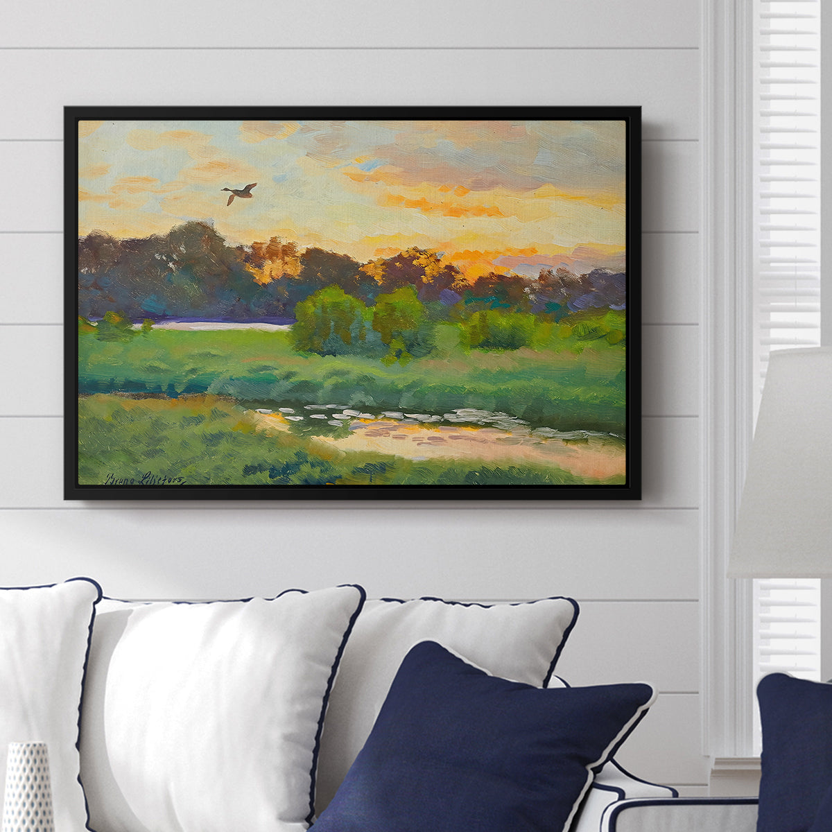 Flying Duck at Sunset, 1924 by Bruno Liljefors displayed above a sofa in a living room in a black floater frame, featuring a lone duck soaring over a glowing marshland.