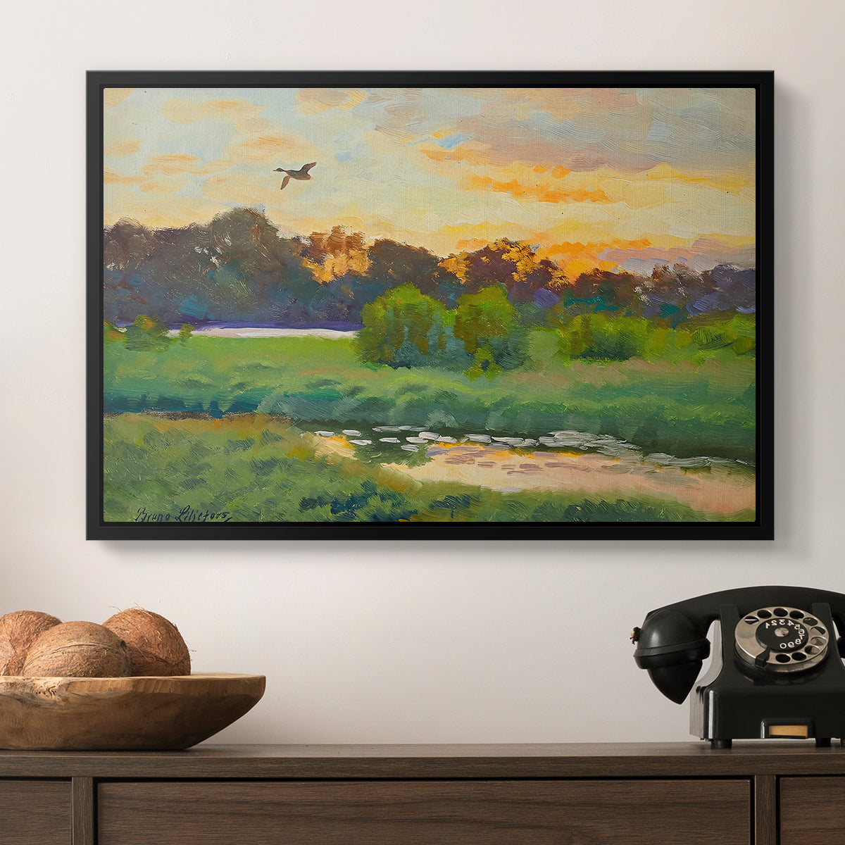Flying Duck at Sunset, 1924 by Bruno Liljefors in a black floater framed canvas displayed above a console table in a hallway, featuring a lone duck flying over a marsh at golden hour.