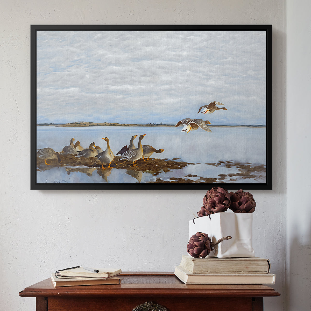 Black floater framed canvas featuring Greylag Geese (Grågäss), 1922 by Bruno Liljefors above an entryway table in a minimalist foyer.