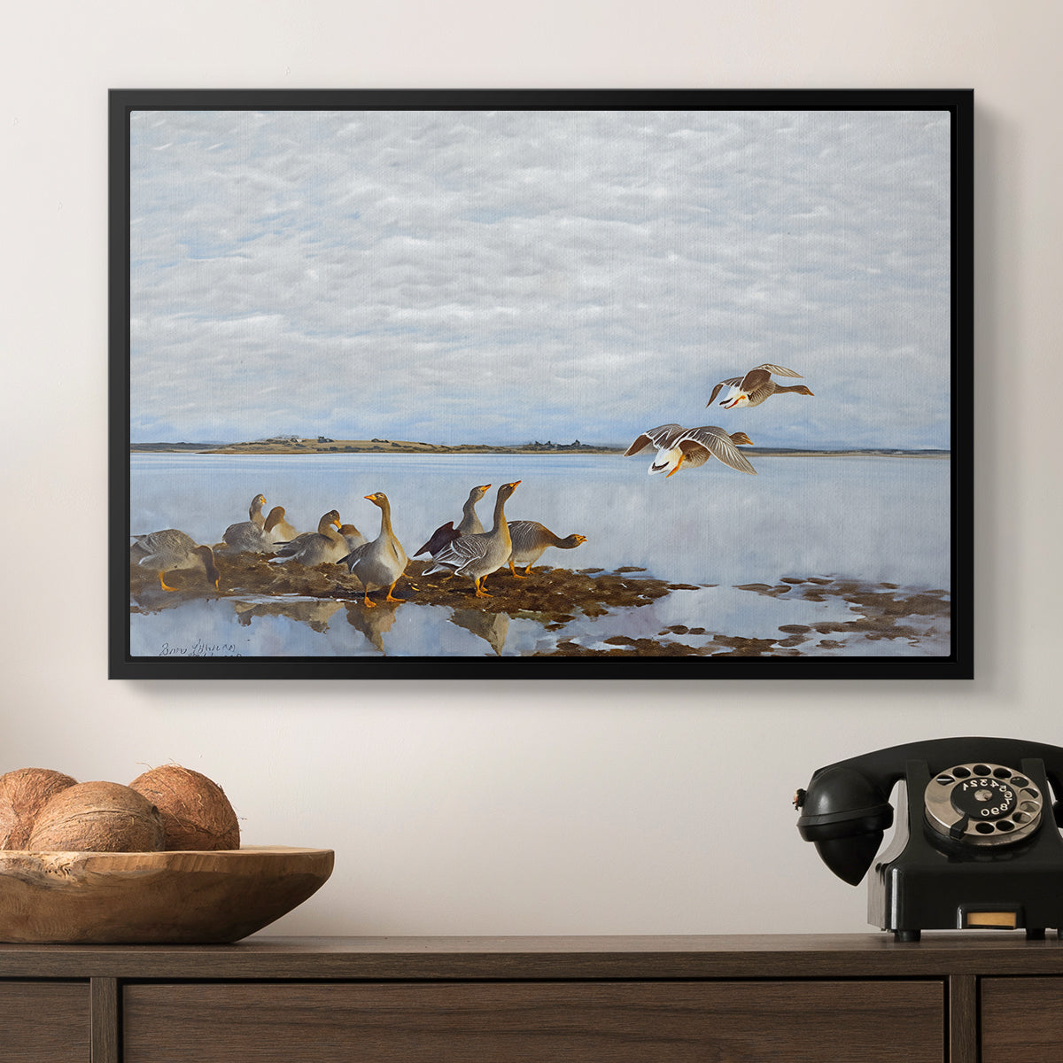 Greylag Geese (Grågäss), 1922 by Bruno Liljefors in a black floater framed canvas displayed above a console table in a hallway, featuring a flock of geese positioned along marshy terrain.
