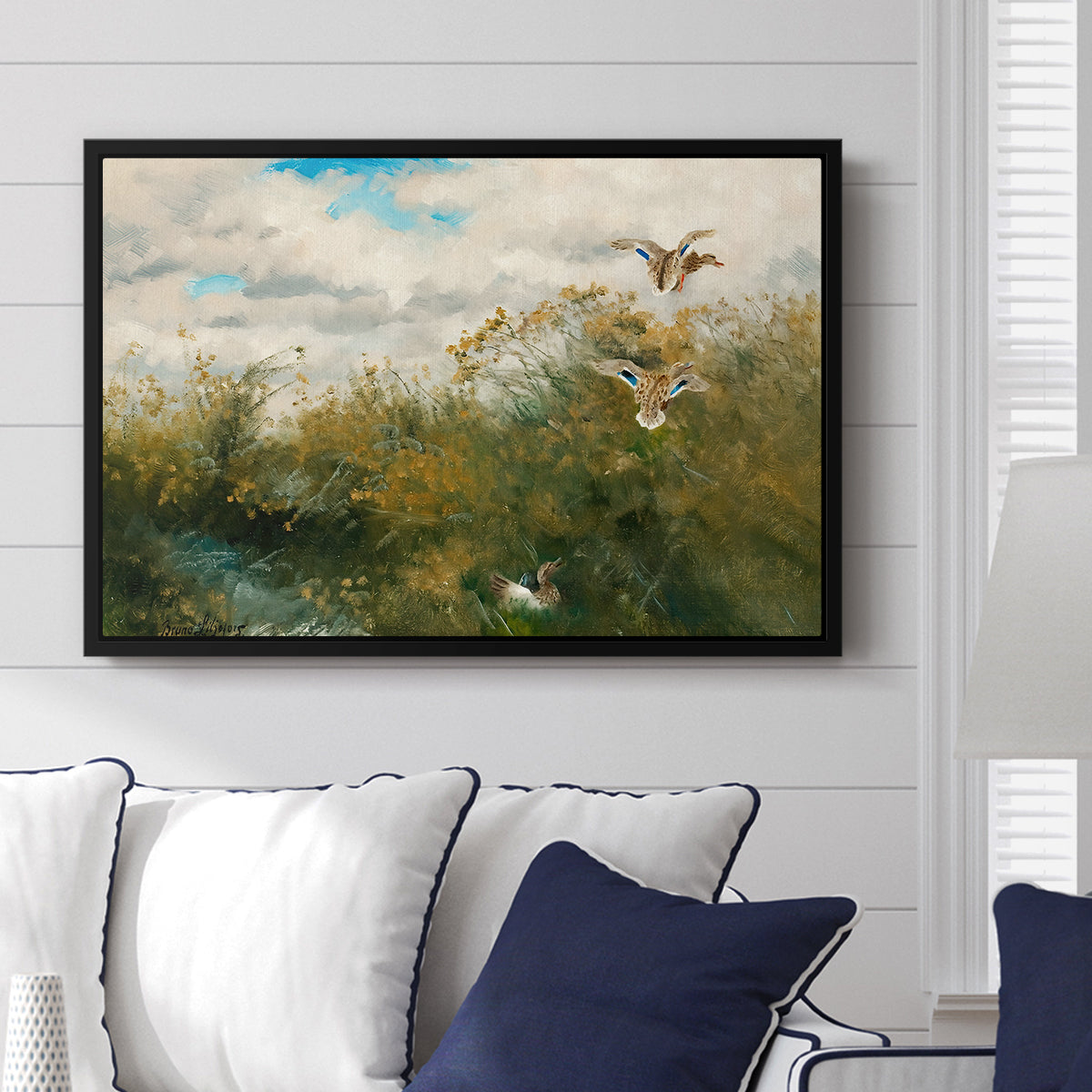 Wild Ducks (Grasänder), 1890 by Bruno Liljefors displayed above a sofa in a living room in a black floater frame, featuring a wildlife scene of ducks walking through tall grass beside water.