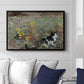 Cat on a Flowery Meadow, 1887 by Bruno Liljefors displayed above a sofa in a living room in a black floater frame, featuring a small cat resting among colorful flowers in grassy field.