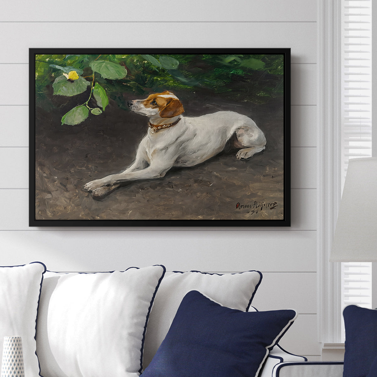 Portrait of a Dog, 1891 by Bruno Liljefors displayed above a sofa in a living room in a black floater frame, featuring a realistic portrait of a resting dog with attentive expression.