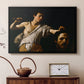 Black floater framed canvas featuring a Baroque depiction of youth holding severed head in shadowy setting, displayed above a cabinet in a soft-toned living room.