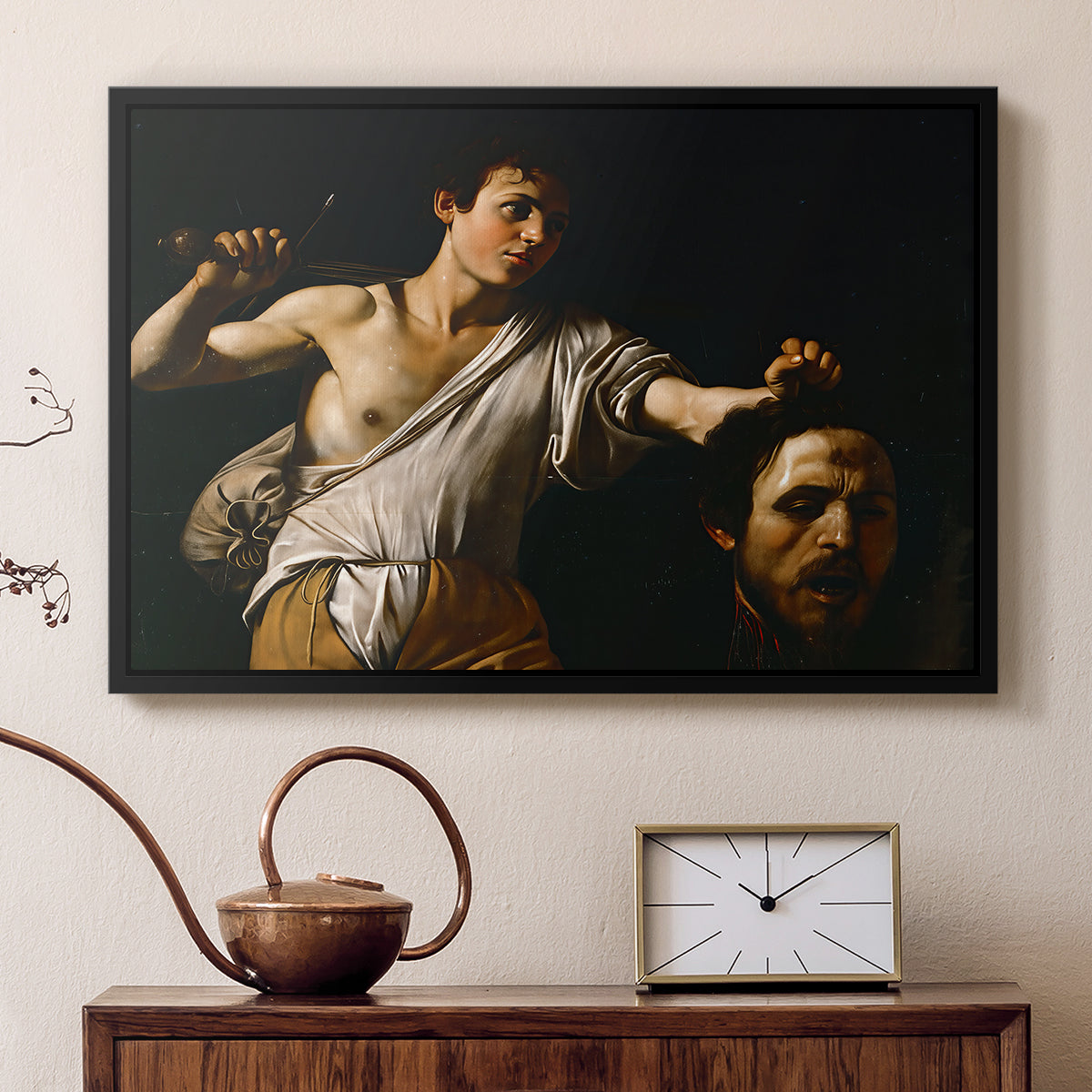 Black floater framed canvas featuring a Baroque depiction of youth holding severed head in shadowy setting, displayed above a cabinet in a soft-toned living room.