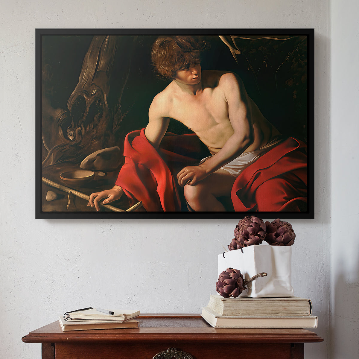 Black floater framed canvas featuring Saint John the Baptist in the Wilderness, c. 1603-1604 by Caravaggio above an entryway table in a minimalist foyer.