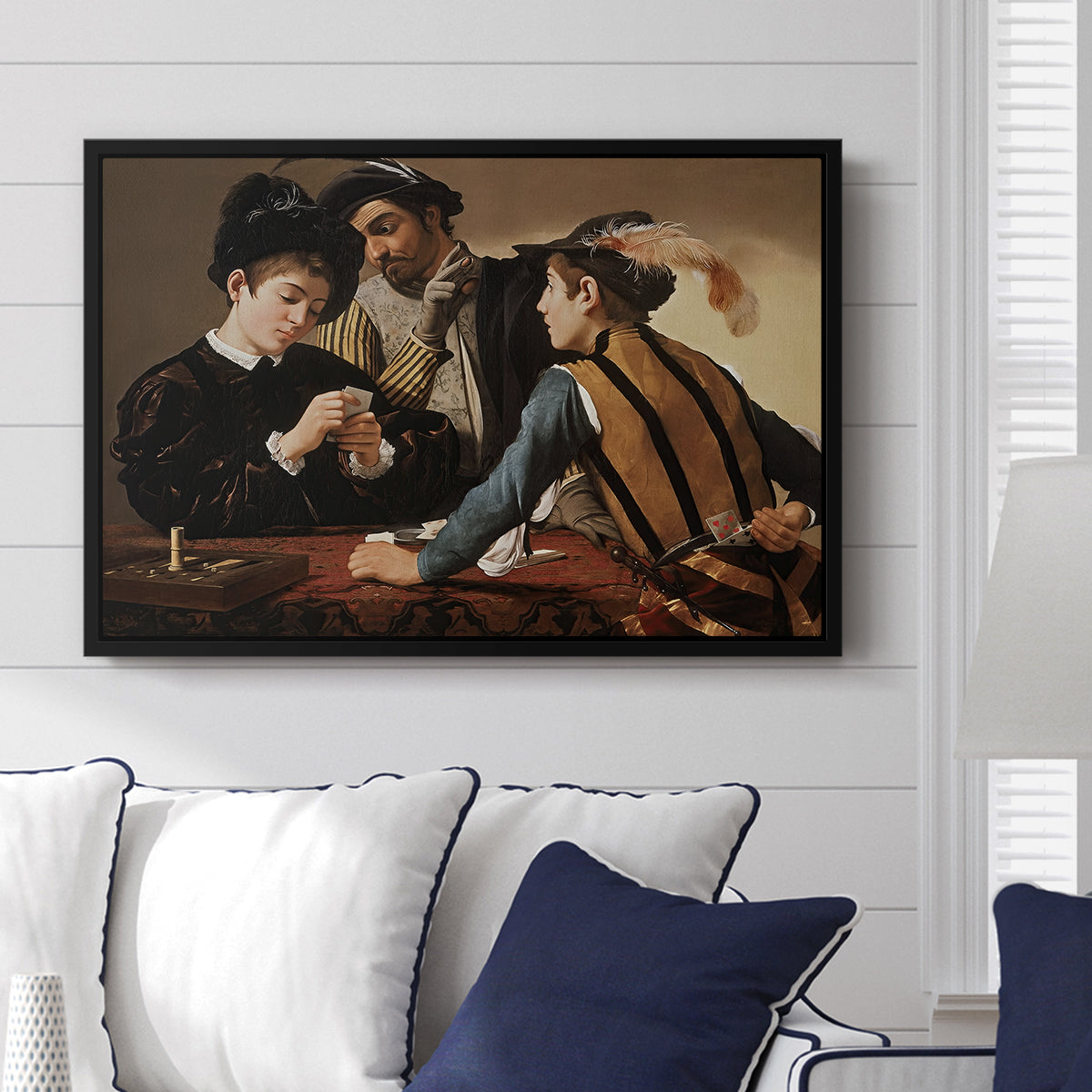 The Cardsharps, c. 1594 by Caravaggio displayed above a sofa in a living room in a black floater frame, featuring a genre scene of card game with deception and hidden accomplice.